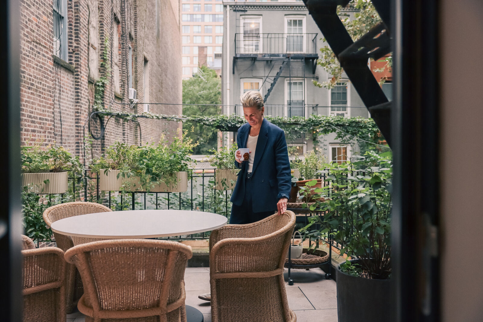Albi Zhubi standing at a rooftop terrace table in a navy suit, holding a cup