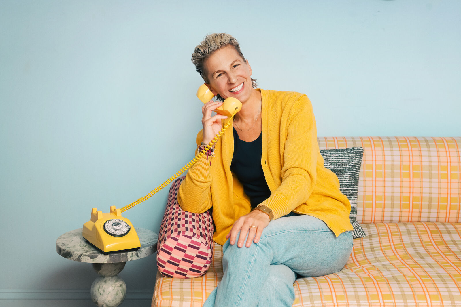 Albi Zhubi on a patterned sofa, smiling into a yellow rotary phone